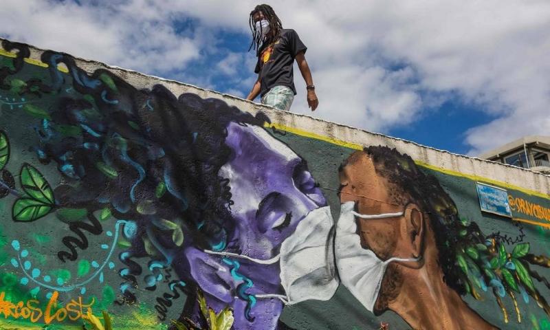 Um homem caminha acima da pintura mural do grafiteiro Marcos Costa: Covid-19. Foto: Antonello Veneri / AFP (clique e veja mais fotos)